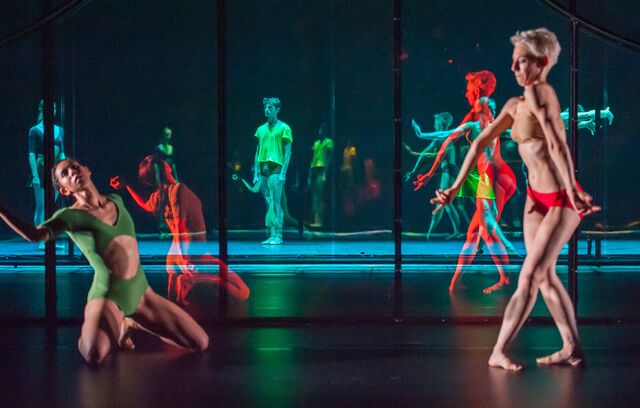 Two dancers in florescent leotards and trunks are reflected in the mirror set, multiplying their image countless times